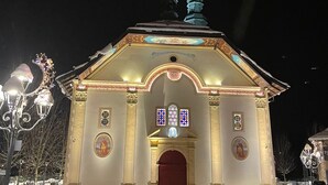 Lumipeitteinen rakennus, jossa on punainen ovi, ja sen edessä oleva lumipeitteinen katu, jotka valaistaan katulamppujen valolla.