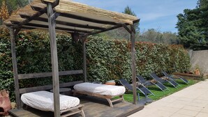 Eine hölzerne Pergola mit zwei Betten, einem kleinen Tisch und einem Stuhl.