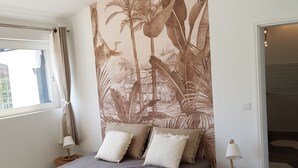 Ein Schlafzimmer mit Bett, Nachttisch, Lampe, Fenster mit Vorhängen und Wandgemälde.