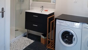 Ein modernes Badezimmer mit einer gläsernen Duschkabine, einem weißen Waschbecken mit Spiegel darüber und einer Frontladewaschmaschine.