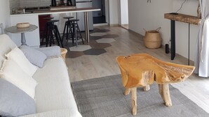 Eine moderne Küche mit weißen Schränken, einer Mikrowelle und einem Kühlschrank. Ein Essbereich mit einem Holztisch und Stühlen ist vorhanden. Ein Fernseher ist an der Wand montiert und ein Zimmerpflanze steht auf einem Regal.