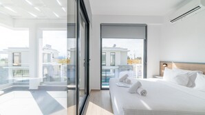 Une chambre d’hôtel moderne avec un grand lit, un balcon doté d’une porte vitrée et une vue sur d’autres immeubles.