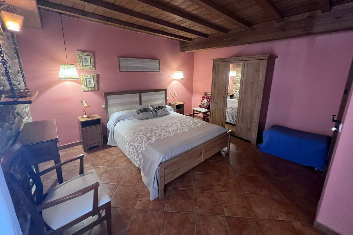 A bedroom with a bed, wooden headboard, bedside tables, a chair, a wardrobe, and a blue bench.