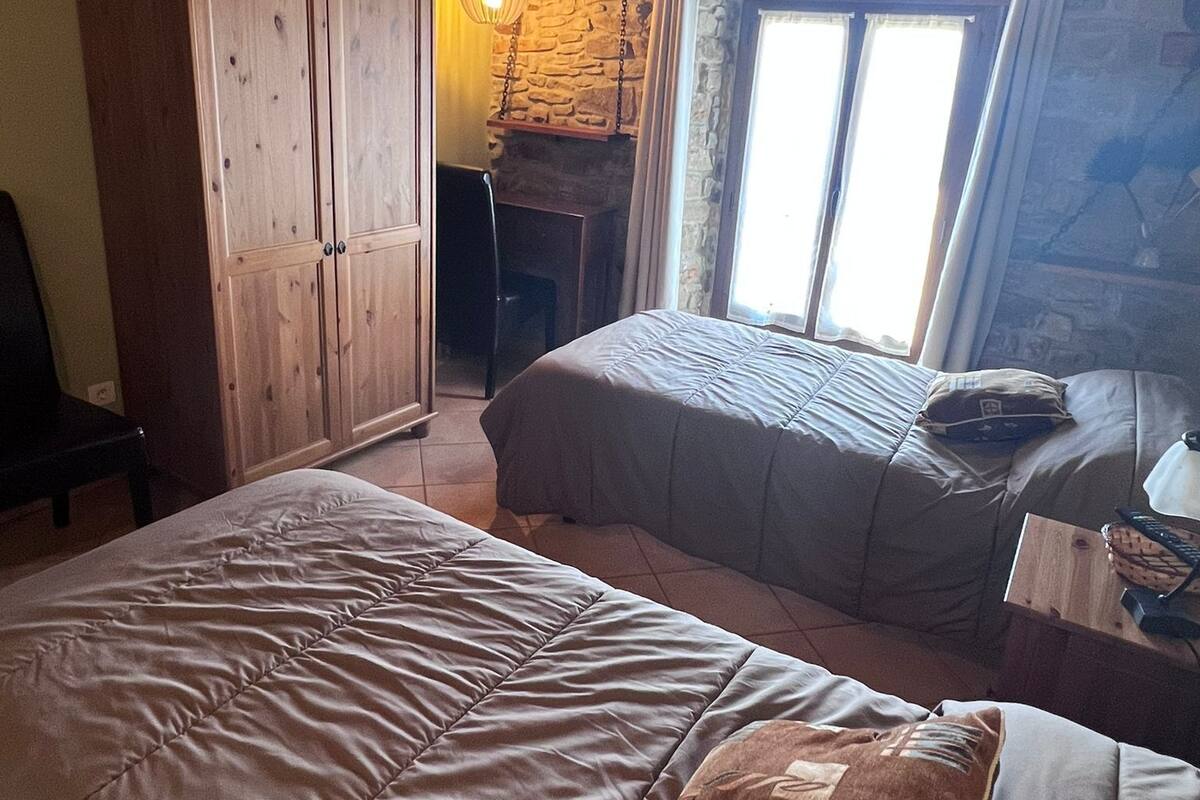 A bedroom with two beds, wooden wardrobe, stone wall, and a window with curtains.