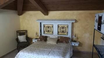 A bedroom with a bed, two nightstands, a chair, and a shelf with decorative items.