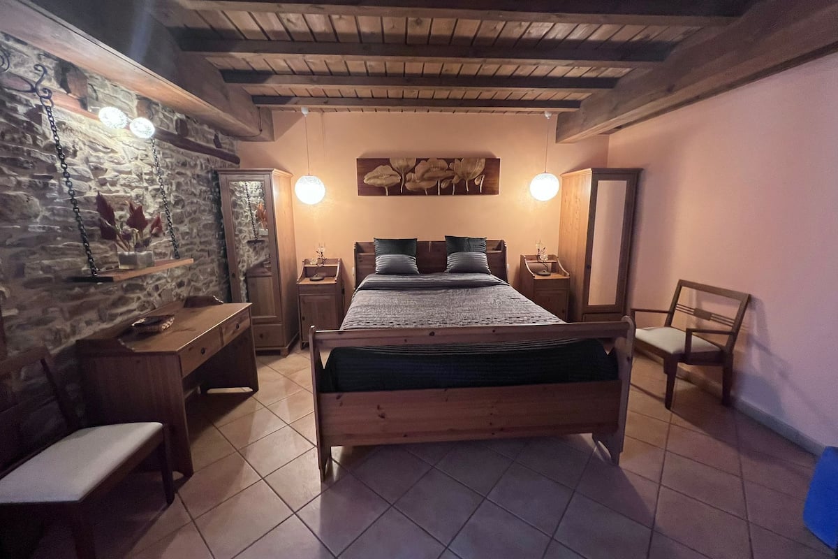 A bedroom with a wooden bed, a desk, a chair, and a nightstand.