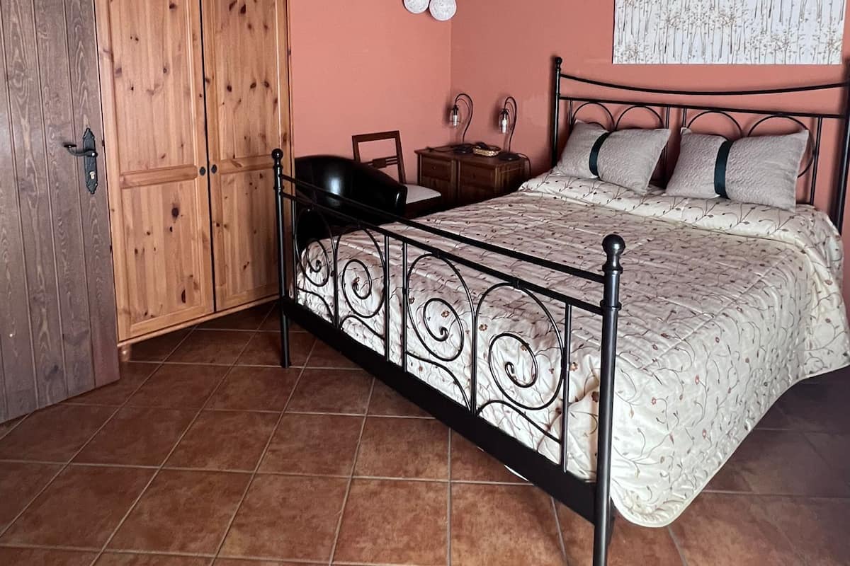 A bedroom with a metal bed frame, wooden wardrobe, and a pink wall.