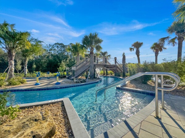 Relax by the serene pool surrounded by lush greenery and palm trees, with a small bridge offering access to the water.