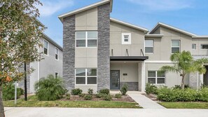 A modern two-story building with a stone facade, multiple windows, and a well-maintained front yard with various plants. - Storey Lake Resort 5 Bedroom Townhome Pet Friendly (Kissimmee)