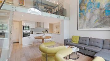 Un intérieur moderne comprenant un espace repas, une cuisine et un salon, avec une chambre en mezzanine dotée d’une rambarde en verre.