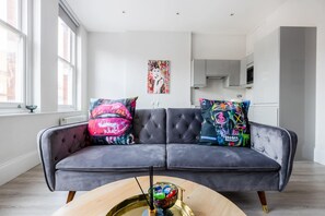A modern living room with a grey sofa, colorful cushions, and a glass coffee table.