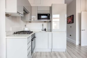 A modern kitchen with white cabinetry, a gas stove, a microwave, and a sink.