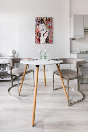 A modern dining area with a round table, two chairs, and a colorful abstract painting on the wall.