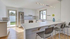 Een moderne keuken met witte kasten, een roestvrijstalen koelkast, een oven, een wasmachine en een groot eiland met barkrukken.