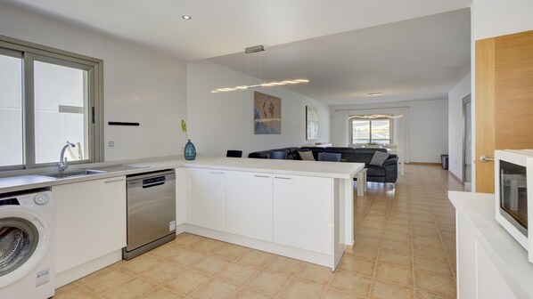 A modern kitchen with a dishwasher, washing machine, and a dining area with a sofa and table. - Cindy Luxury Villa (Antigua)