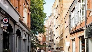 Eine enge Straße mit Außenbestuhlung, Backsteingebäuden und Fußgängern.
