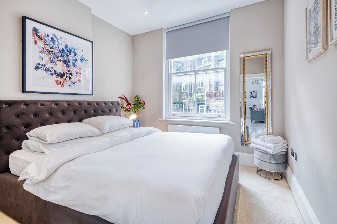 Un dormitorio con una cama grande, una ventana con vistas, un espejo y una obra de arte enmarcada en la pared.
