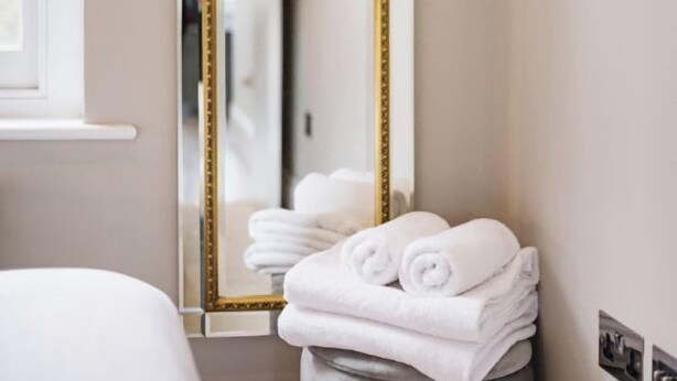 Un bagno con uno specchio grande, una pila di asciugamani bianchi e una finestra.