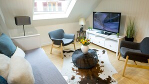 A modern living room with a sloped ceiling, a television, a sofa, two chairs, a small table with a vase of flowers, and a cowhide rug. - Les Tournesols **, 2-bedroom 2-bathroom apartment in the historic heart of Kaysersberg (Kaysersberg-Vignoble)