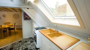 A kitchen with a skylight, wooden cabinets, a sink, and a dining area with chairs and a table. - Les Tournesols **, 2-bedroom 2-bathroom apartment in the historic heart of Kaysersberg (Kaysersberg-Vignoble)