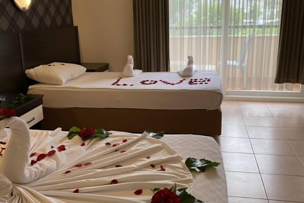 A hotel room with a bed, a massage table, and a view of the outdoors through large windows.