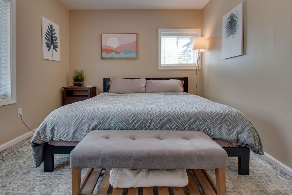 Ein Schlafzimmer mit Bett, Sitzbank, Nachttisch, Lampe und Wandbild.
