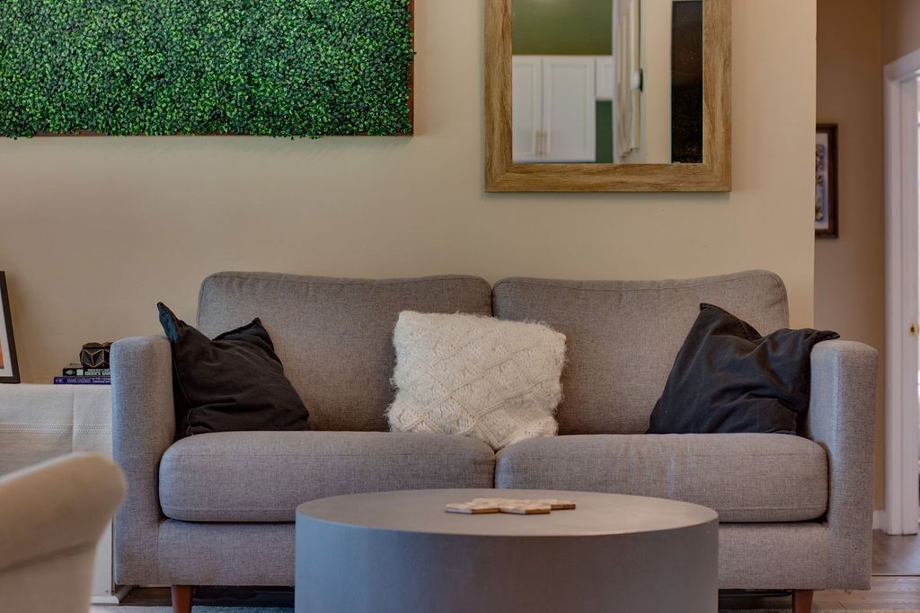 A living room with a grey sofa, a round coffee table, and a green wall decoration.