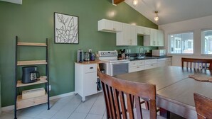 Une cuisine avec des meubles blancs, une table à manger en bois et un mur vert.