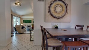 Un coin repas avec une grande table et des chaises en bois, une peinture abstraite moderne accrochée au mur et une vue sur le salon.