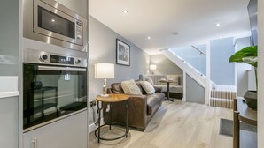 A modern kitchen with a built-in microwave and oven, a round wooden table, a leather sofa with cushions, and a staircase leading to an upper level. - The Old School House & Rooms- The Lace Market  (Nottingham)