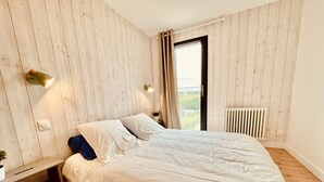 Ett sovrum med en säng, träväggar, ett element och ett fönster med gardiner.