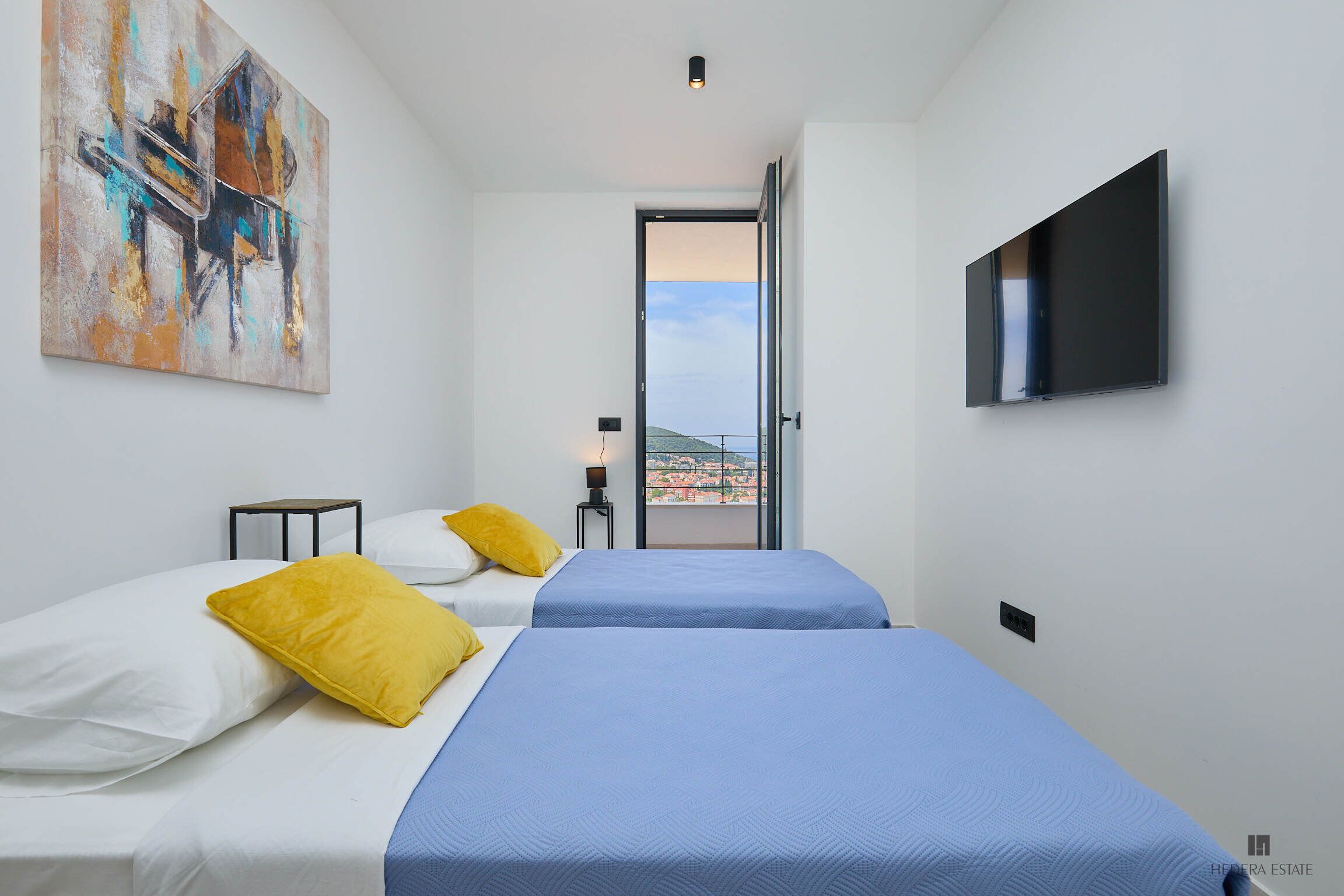 Une chambre d’hôtel avec deux lits, un tableau au mur, un téléviseur fixé au mur et un balcon avec vue.
