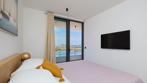 Ein Hotelzimmer mit Bett, Fernseher, einem Gemälde und Blick auf Stadt und Wasser.
