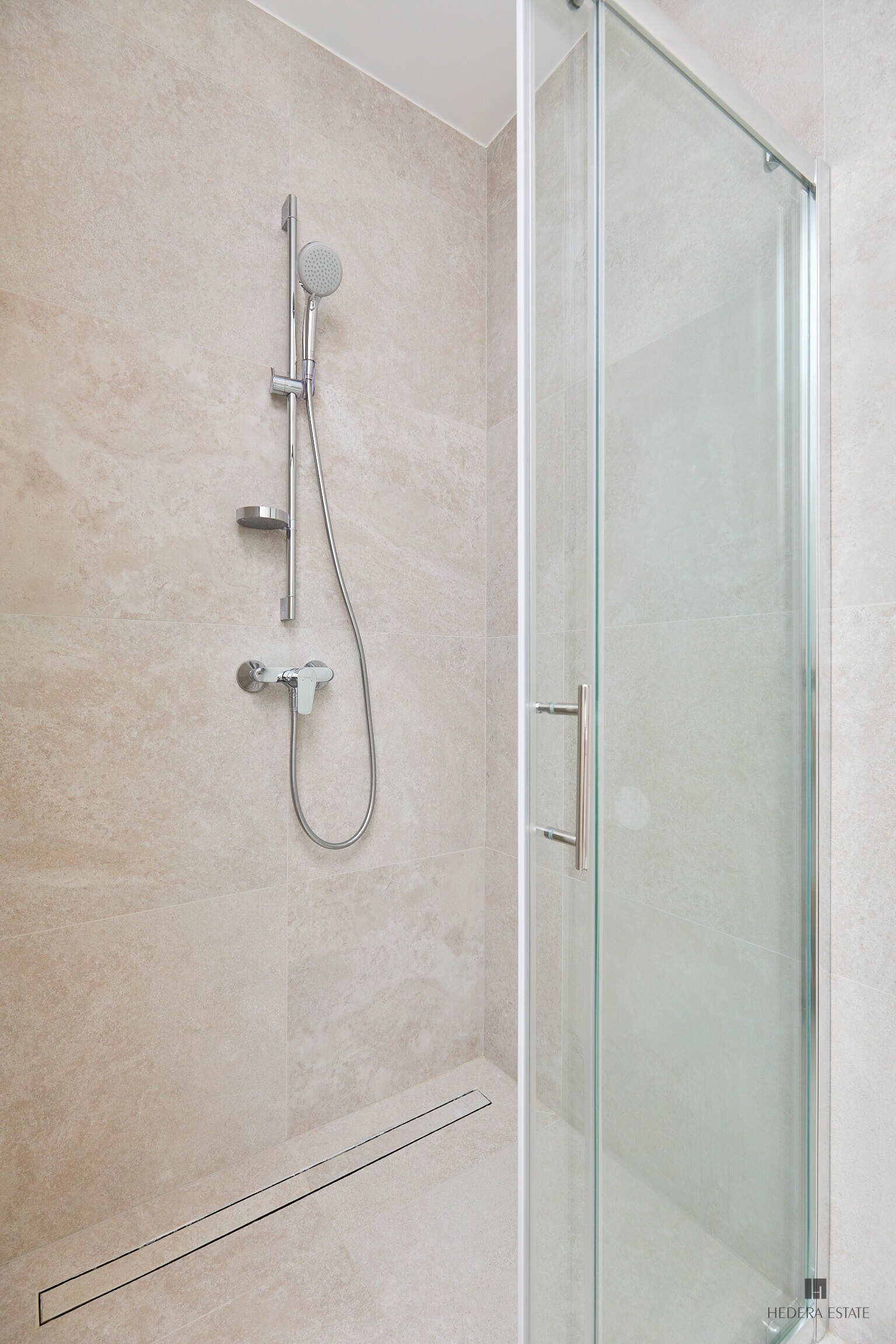 A modern bathroom with a glass shower enclosure, a handheld showerhead, and a wall-mounted faucet.