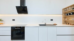 Eine moderne Küche mit weißen Schränken, einem eingebauten Backofen, einer schwarzen Dunstabzugshaube und einem Holzregal mit Küchenutensilien.