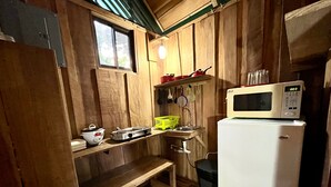 A compact kitchen with wooden walls, a window, a microwave, a sink, and a small table.