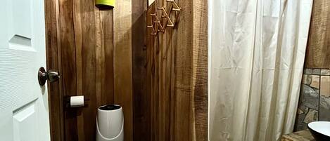 Un baño de madera con suelo de piedra, inodoro, bidé y cortina de ducha.