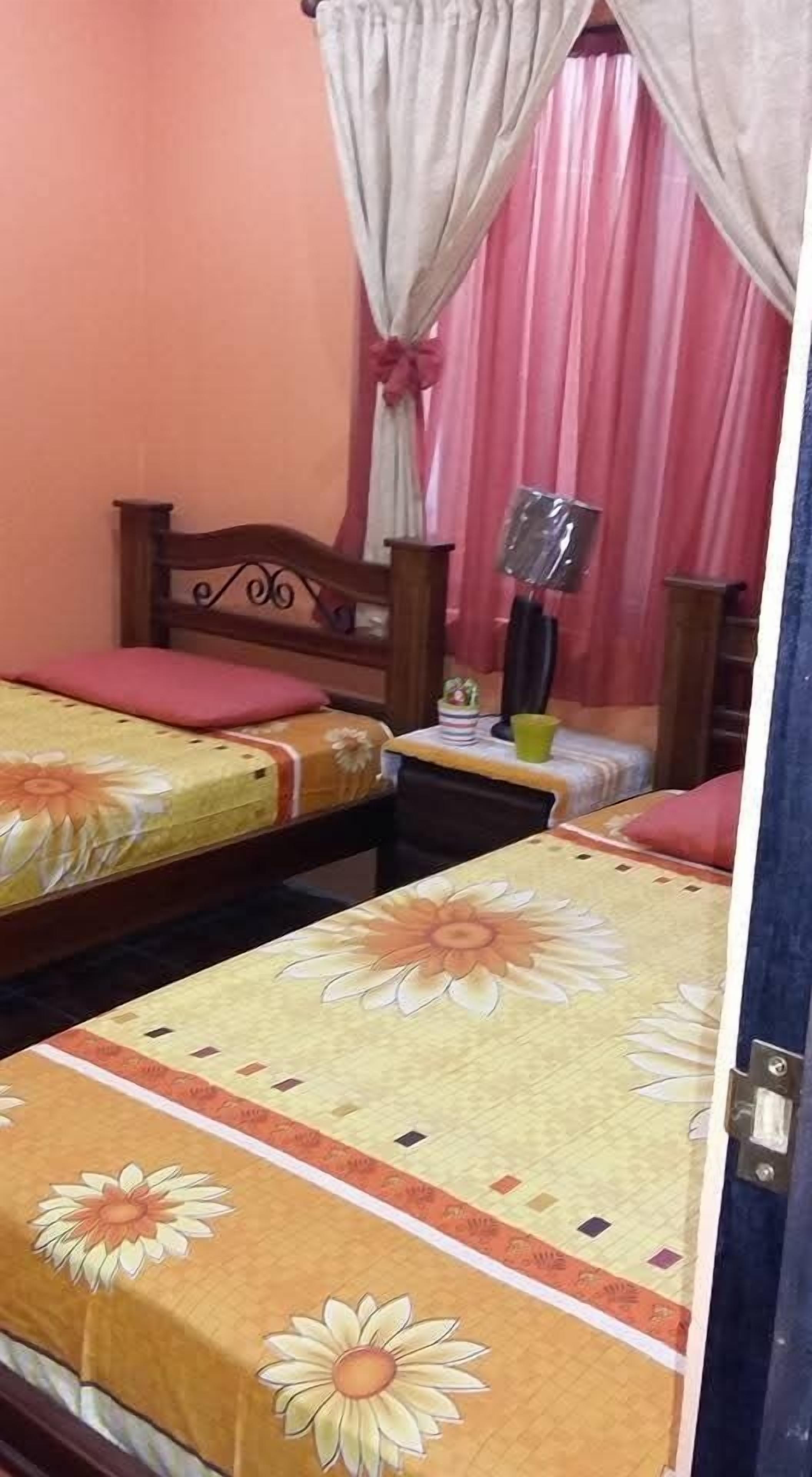 Une chambre à coucher avec deux lits, chacun recouvert d’une couvre-lit à motifs floraux, doté d’une tête de lit en bois et agrémenté d’une table de chevet avec une lampe.