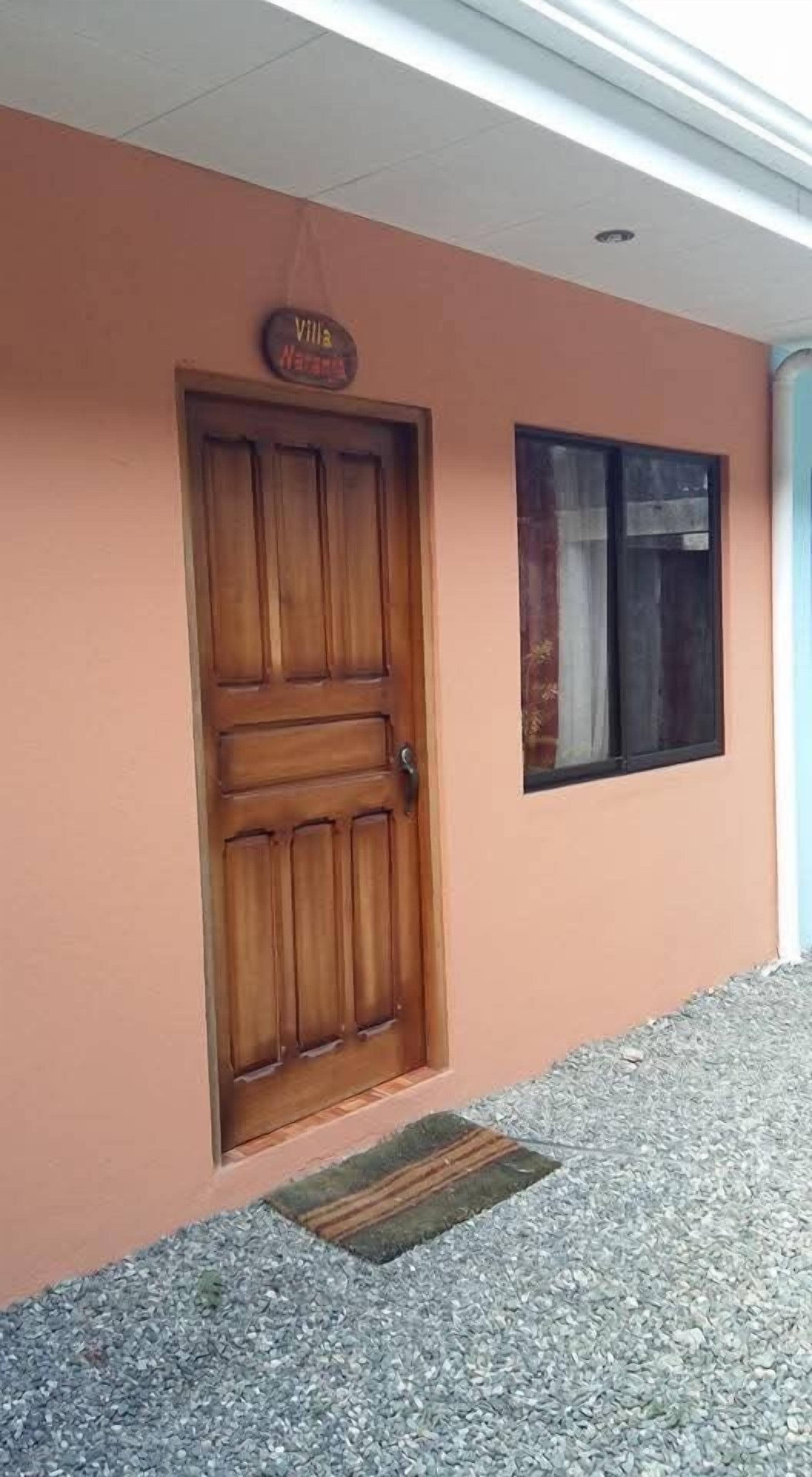 A wooden door with a sign above it, a window with a curtain, and a doormat in front of the door.