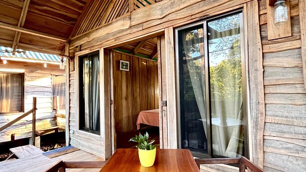 A wooden cabin with a covered patio, a table with a potted plant, and large sliding glass doors.