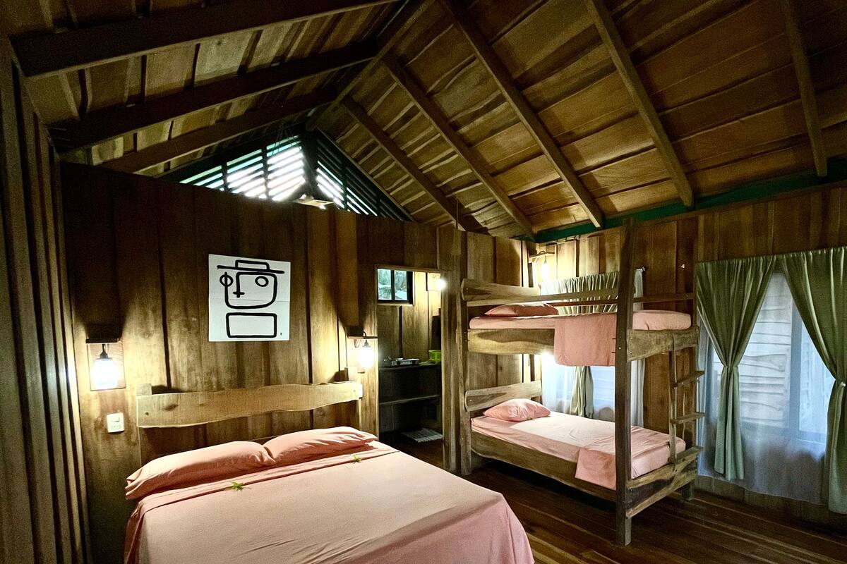 Ein Zimmer mit Holzwänden und einer geneigten Decke, ausgestattet mit Etagenbetten, einem Schreibtisch mit Stuhl und einem Fenster mit Vorhängen.