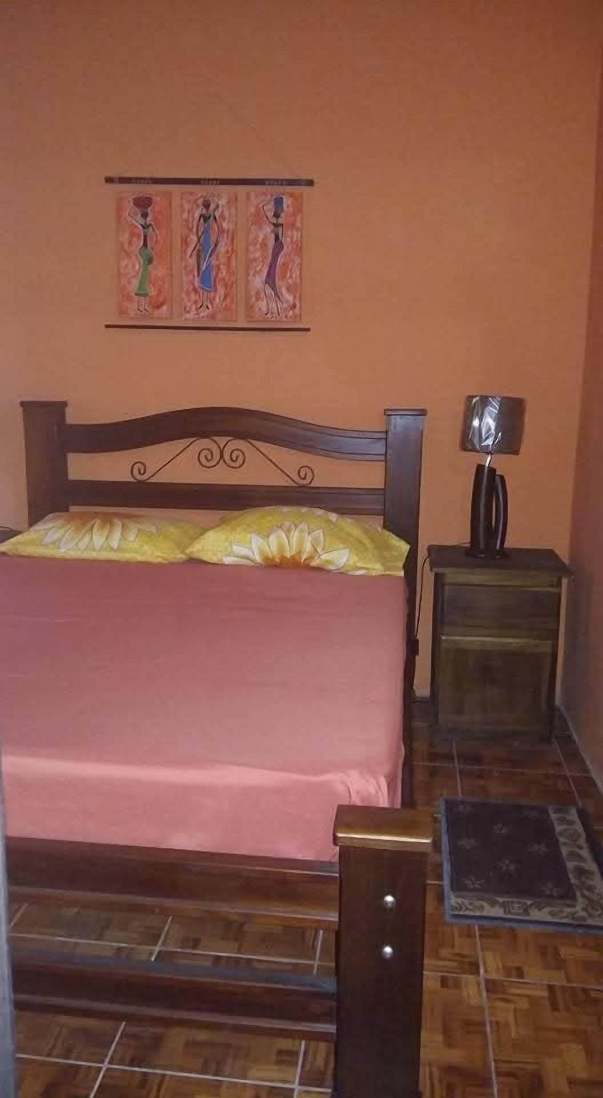 Ein Schlafzimmer mit einem hölzernen Bett, einem Nachttisch mit Lampe und einem Gemälde an der Wand.