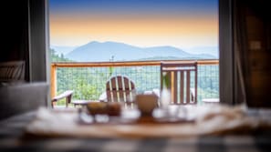 A room with a view of mountains through a window. There are two chairs and a table in the foreground.