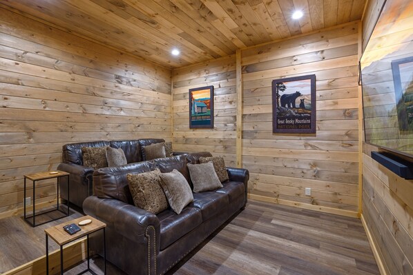 A cozy room with a leather sofa, wooden walls, and a poster of the Great Smoky Mountains National Park.