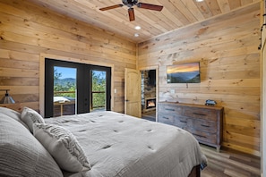 A wooden-paneled bedroom with a bed, a fireplace, a television, and a view of the outdoors.
