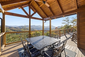 A wooden deck with a table and chairs, overlooking a mountainous landscape.