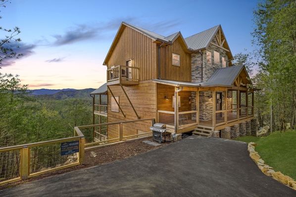 A large wooden cabin with a stone extension, a covered porch, and a view of the surrounding forest.