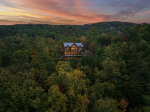 A large, two-story wooden cabin surrounded by dense forest, with a prominent balcony and multiple windows. - The Hidden Owl Mountain Lodge 5 Bedroom Cabin by RedAwning (Sevierville)