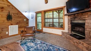 A cozy living room with a fireplace, a mounted deer head, and a large window with blinds. - Whitetail Cabin 2 Bedroom Cabin by RedAwning (Gatlinburg)