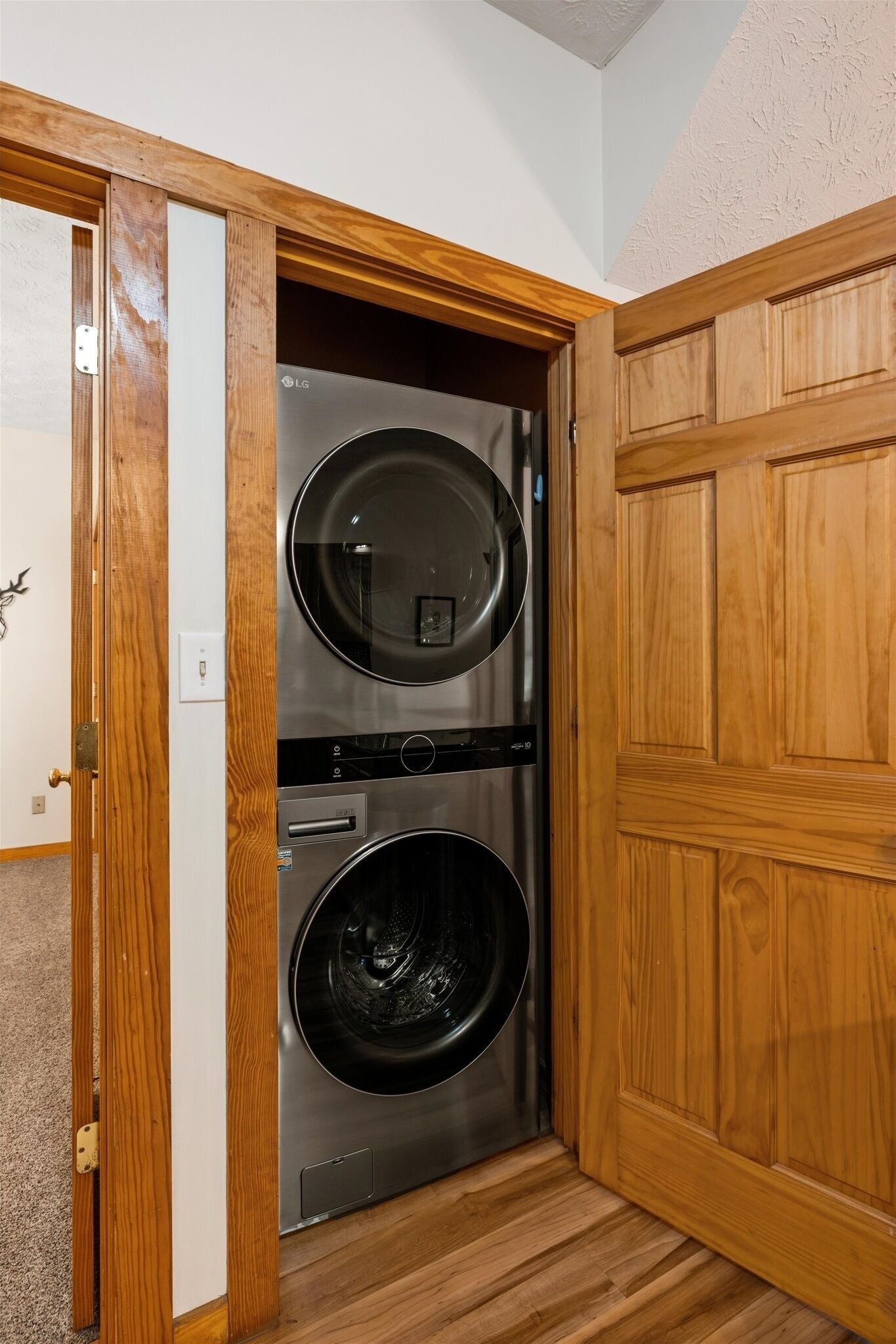 A compact laundry room with a built-in washer and dryer, wooden cabinetry, and a door with a brass handle.